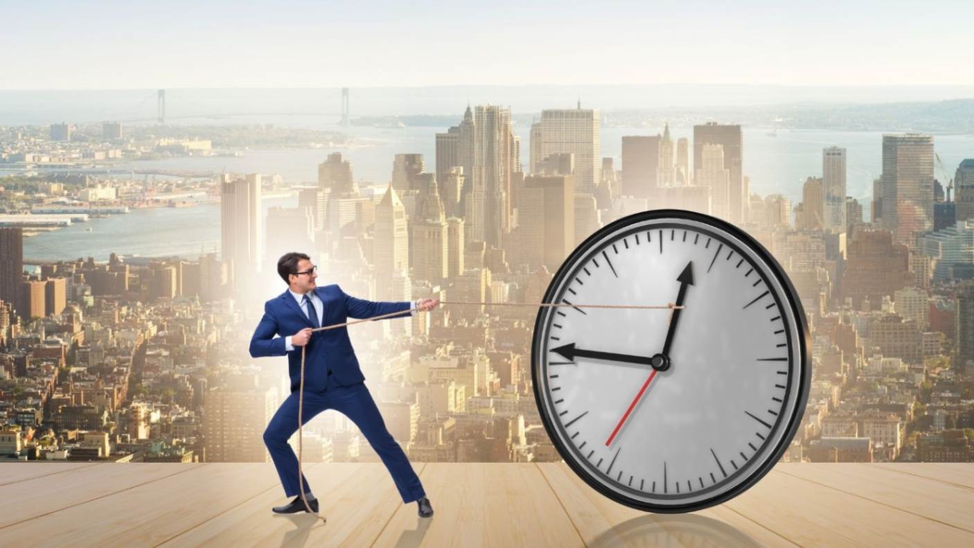 Time management man in blue suit pulling big clock on a skyscraper background