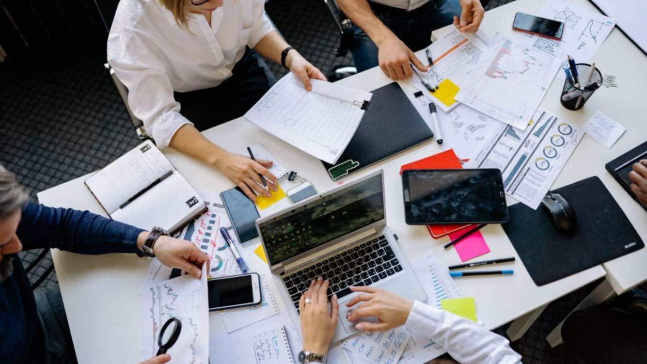 ability to work as a team men and women sitting around a desk interacting with project documents