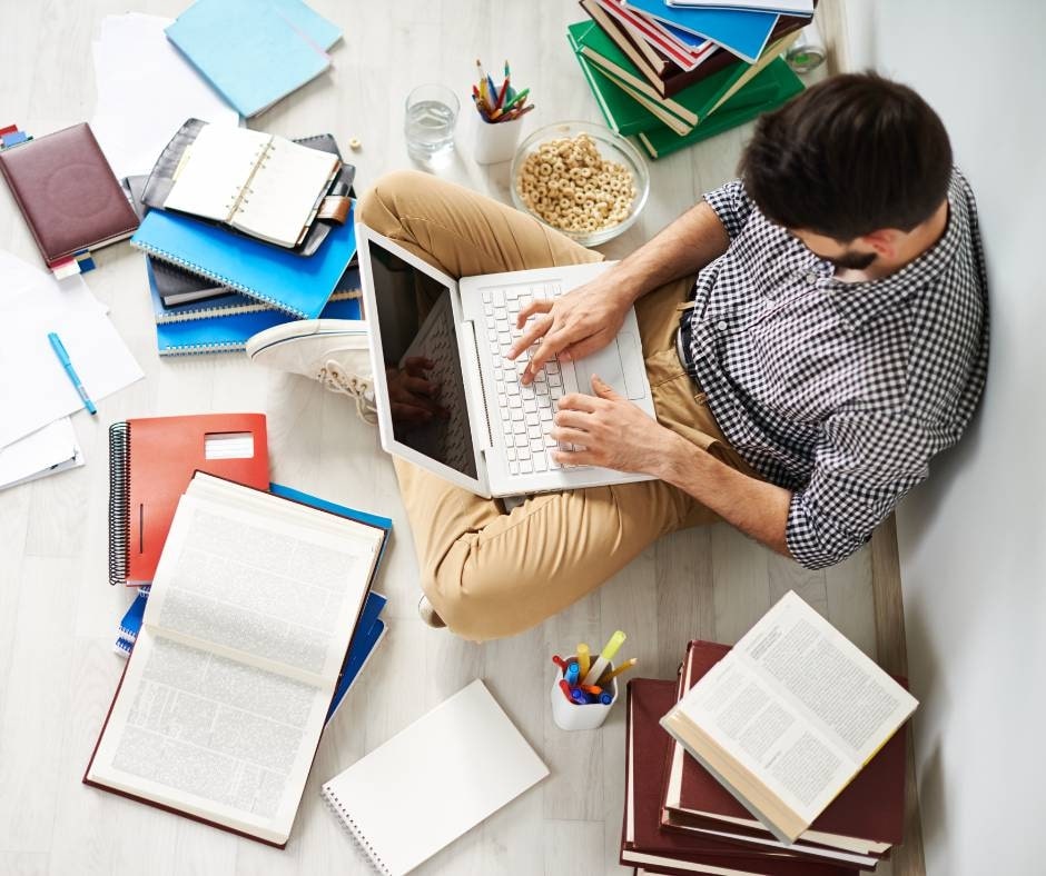 research skills man with laptop sitting on floor surrounded by lots of research books