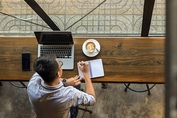 man sitting with laptop writing in a note pad with a coffee